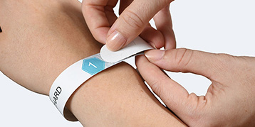 Eine Hand legt ein Einlassband an einem Arm an.