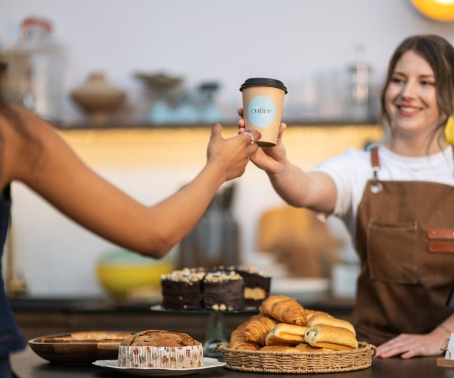 Eine Frau übergibt einen Kaffeebecher, auf dem ein Etikett klebt.