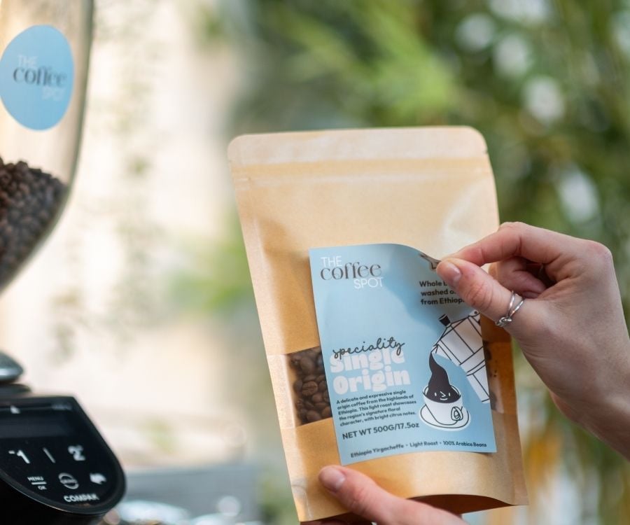 Eine Hand klebt ein rechteckiges Etikett auf eine Kaffee-Packung.