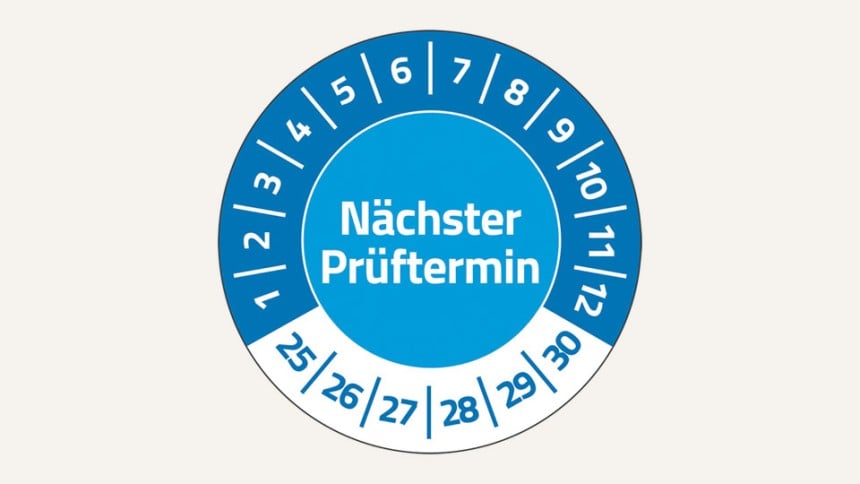 Man sieht eine runde Prüfplakette In der Mitte steht "Nächster Prüftermin". Oben im Halbkreis stehen in Weiß die Zahlen 1 bis 12. Unten stehen die Zahlen 25 bis 30.