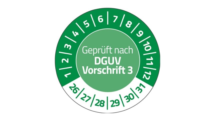 Eine grüne Prüfplakette. In der Mitte steht "Geprüft nach DGUV Vorschrift 3". Im Halbkreis stehen die Zahlen 1 bis 12. Unten stehen die Zahlen 26 bis 31.