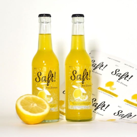 Transparente Flaschenetiketten kleben auf zwei Limonaden-Flaschen. Im Hintergrund ist ein Bogen mit transparenten Etikettn.