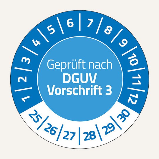 Man sieht eine runde Prüfplakette. In der Mitte steht der Text "Geprüft nach DGUV Vorschrift 3". Im oberen Bereich stehen im Halbkreis die Zahlen 1 bis 12. Unten stehen die Zahlen 25 bis 30.