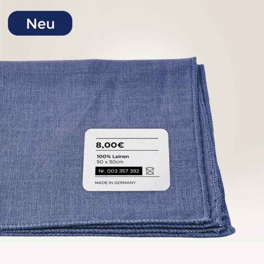 Eine blaue Decke ist zusammengelegt. Auf der Decke klebt ein Textilaufkleber mit weiteren Informationen, wie Preis und Materialinformationen. In der linken Ecke oben ist ein "NEU"-Hinweis.