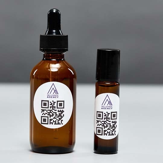 Auf zwei Arzneifläschchen kleben runde Etiketten mit einem QR-Code und dem Firmenlogo.