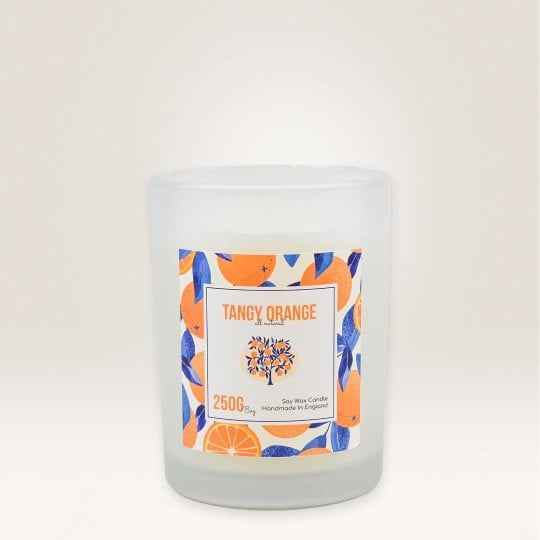 Auf einem Kerzenglas klebt ein Etikett auf dem Tangy Orange steht. Im Hintergrund ist ein Muster aus Orangen zu sehen.
