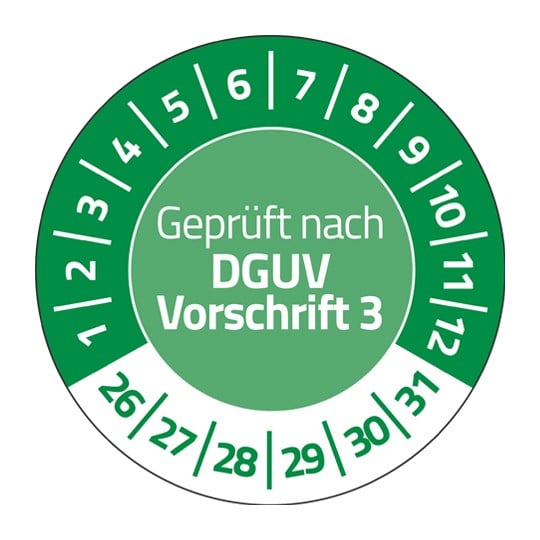 Eine grüne Prüfplakette. In der Mitte steht "Geprüft nach DGUV Vorschrift 3". Im Halbkreis stehen die Zahlen 1 bis 12. Unten stehen die Zahlen 26 bis 31.