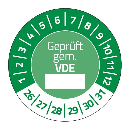 Eine grüne Prüfplakette. In der Mitte steht "Geprüft gem. VDE", darunter ein weißer Kasten. Im Halbkreis stehen die Zahlen 1 bis 12, unten die Zahlen 26 bis 31.