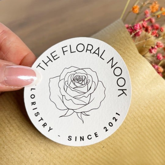 Auf einem Baumwoll-Papier-Aufkleber ist ein florales Motiv abgebildet. Er wird auf die Verpackung eines Blumenstraußes geklebt.
