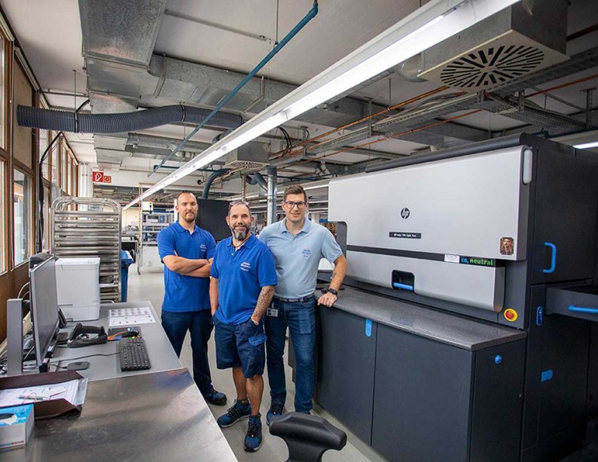 Drei Männer stehen in der Digitaldruckabteilung vor den Druckmaschinen. Promobild für Karriere in der Produktion und Logistik.
