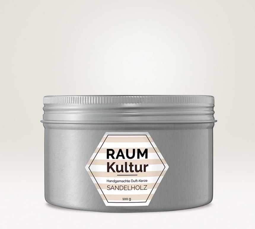 Auf einem silbernen Behältnis klebt ein sechseckiges Kerzenetikett. Auf dem Kerzenetikett steht "Raumkultur handgemachte Duft-Kerze Sandelholz".