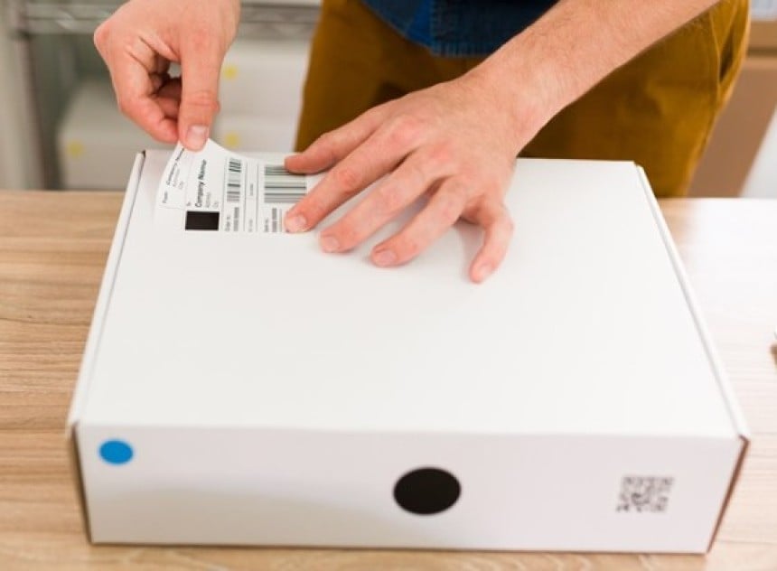 Bedrucktes Versandetikett wird auf weißes Paket aufgebracht.