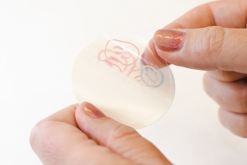 Ein transparenter Einzel-Aufkleber wird von zwei Fingern gehoben.