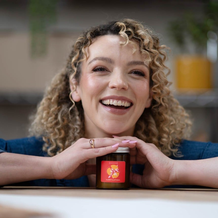 Frau lacht und hält mit zwei Händen ein Produktglas.