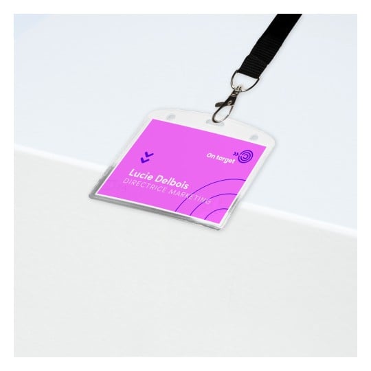 Das Bild zeigt ein Namensschild auf einer weißen Fläche. Das Schild ist pink und trägt den Namen 'Lucie Delbois' und den Titel 'DIRECTRICE MARKETING'. Es hat einen Clip, der an einem schwarzen Band befestigt ist.