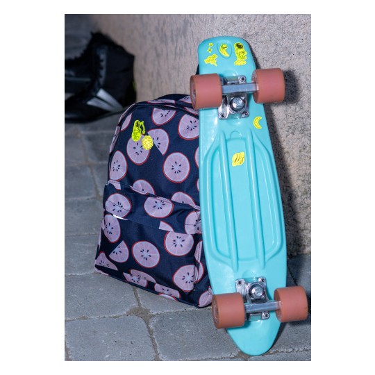 Ein türkisfarbenes Skateboard lehnt an einem Rucksack mit Fruchtmuster.
