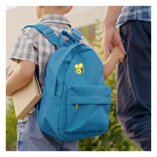 Ein Kind hält ein Buch und geht Hand in Hand mit einem Erwachsenen. Das Kind hat einen blauen Rucksack mit einer gelben Cartoonfigur darauf.