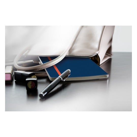 Das Bild zeigt eine stilvolle Handtasche, die teilweise geöffnet ist und ein blaues Notizbuch mit einem roten Streifen, einen Stift und einige Kosmetikartikel wie Lippenstift und Nagellack auf einer reflektierenden Oberfläche enthüllt.