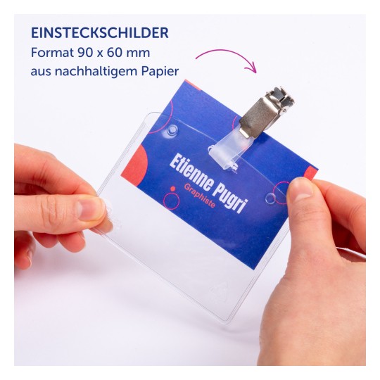 Das Bild zeigt eine Person, die ein Namensschild hält, das den Namen "Etienne Pugri" trägt und angibt, dass es aus nachhaltigem Papier hergestellt ist. Das Schild hat einen Clip zur Befestigung.