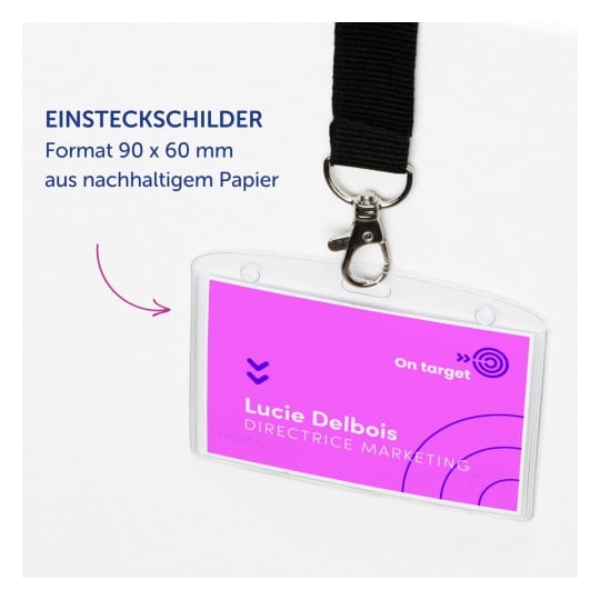Das Bild zeigt ein Namensschild mit einem rosa und lila Design, auf dem der Name 'Lucie Delbois' und der Titel 'MARKETINGDIREKTORIN' abgebildet sind. Es hebt nachhaltiges Papiermaterial hervor.