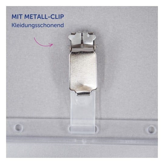 Das Bild zeigt eine Metallklammer, die an einem transparenten Kunststoffhalter befestigt ist. Die Klammer ist mit 'MIT METALL-CLIP' beschriftet und trägt zusätzlichen Text auf Deutsch, der als 'kleidungsfreundlich' übersetzt wird.