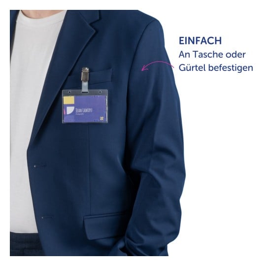 Das Bild zeigt eine Person, die ein dunkelblaues Sakko trägt, mit einem Namensschild, das an der Tasche befestigt ist. Das Schild zeigt den Namen 'JEAN LAMIPU' und das Wort 'Fotograf'. Auf der rechten Seite befindet sich ein Text, der vorschlägt, es an einer Tasche oder einem Gürtel zu befestigen.