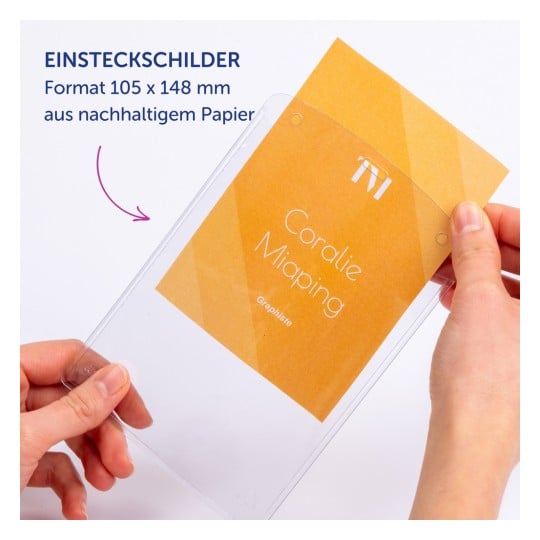 Das Bild zeigt eine Person, die einen transparenten Plastikschilderhalter mit einer eingesteckten Karte hält. Die Karte enthält Text und Farben, die darauf hinweisen, dass sie aus nachhaltigem Papier hergestellt ist. Sie enthält den Namen 'Coralie Miaping' und einige Details über das Format.