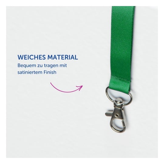 Das Bild zeigt ein grünes Lanyard aus weichem Material mit einem silbernen Clip an einem Ende. Der Text betont seinen Komfort und die satinierte Oberfläche.