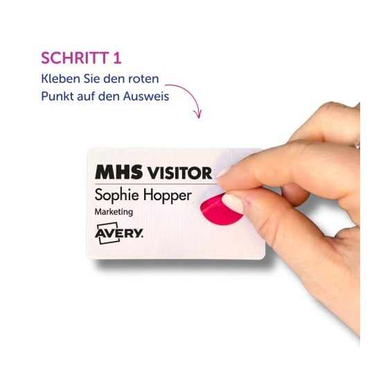 Das Bild zeigt die Hand einer Person, die einen roten Aufkleber auf einen Besucher-Ausweis anbringt. Der Text gibt den Namen Sophie Hopper an, ihre Abteilung als Marketing und die Marke Avery. Ein Schritt mit der Bezeichnung 'Schritt 1' weist darauf hin, den Aufkleber anzubringen.