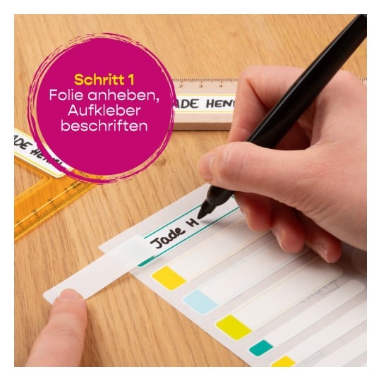 Eine Hand schreibt mit einem schwarzen Marker auf ein Etikett und hebt die Schritte hervor, um eine Folie und Etikettenaufkleber anzuheben. Gelbe und blaue Farbproben sind sichtbar, zusammen mit einem Lineal.