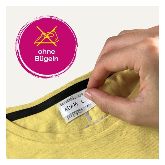 Das Bild zeigt eine Nahaufnahme eines orangefarbenen Kleidungsstücks mit einem Etikett, auf dem 'Manon GIRARD' steht. Es gibt auch eine kreisförmige Grafik, die anzeigt, dass nicht gebügelt werden soll, mit der Aufschrift 'ohne Bügeln' auf Deutsch.