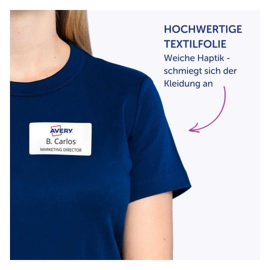Das Bild zeigt eine Person, die ein marineblaues T-Shirt mit einem Namensschild trägt, auf dem "B. Carlos, MARKETING DIRECTOR" steht. Der begleitende Text zum Bild ist auf Deutsch und erwähnt hochwertige Textilfolie und eine weiche Haptik, die sich der Kleidung anpasst.