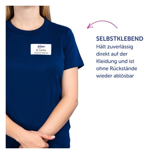 Das Bild zeigt eine Person, die ein dunkelblaues T-Shirt trägt, auf dem ein Namensschild mit der Aufschrift 'B. Carlos, MARKETING DIRECTOR' zu sehen ist. Neben der Person befindet sich ein Text, der eine selbstklebende Eigenschaft der Namensschilder beschreibt.