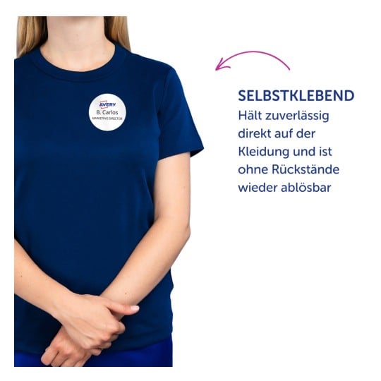 Das Bild zeigt eine Person, die ein dunkelblaues Hemd trägt und ein Namensschild mit der Aufschrift "B. Carlos, Marketing Director" hat. Der Text enthält Informationen über eine selbsthaftende Funktion des Schildes.