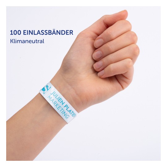Das Bild zeigt eine Hand, die ein weißes Armband trägt, das mit dem Text '100 EINLASSBÄNDER' und 'JULIEN PLATTER MARKETING' beschriftet ist. Das Armband wird als klimaneutral beschrieben.