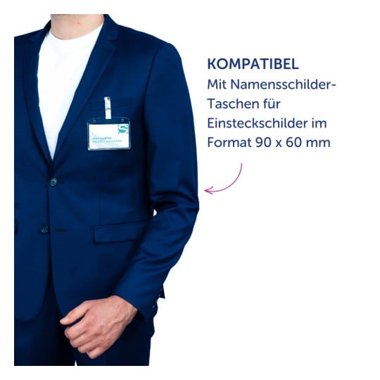 Das Bild zeigt einen Mann in einem blauen Anzug mit einem Namensschild in der Tasche. Auf dem Namensschild steht der Name 'TOM MARTIN' und der Titel 'PROJECT MANAGER'. Ein Text weist darauf hin, dass es mit Namensschildhaltern für Einsätze im Format 90 x 60 mm kompatibel ist.