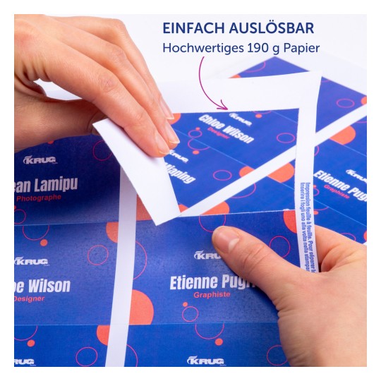 Das Bild zeigt Hände, die eine bedruckte Kartonkarte mit Namen und Bezeichnungen halten, wobei ein Merkmal der einfachen Entfernung hervorgehoben wird und ein farbenfrohes Design zu sehen ist. Der Text auf Deutsch erwähnt hochwertiges Papier.