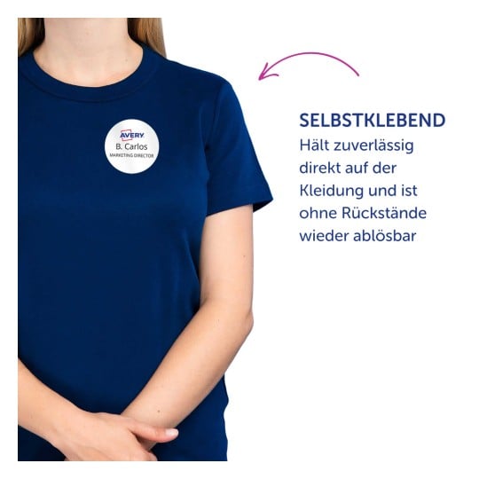 Das Bild zeigt eine Person, die ein marineblaues T-Shirt trägt, mit einem runden Abzeichen, das einen Namen und einen Titel anzeigt. Der Text neben der Person beschreibt ein selbstklebendes Produkt, das an Kleidung haftet und ohne Rückstände entfernt werden kann.