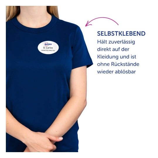 Das Bild zeigt eine Person, die ein marineblaues Hemd trägt, mit einem Namensschild, auf dem 'B. Carlos, Marketing Director' steht. Der Text neben der Person erklärt, dass das Namensschild selbstklebend ist und sich leicht entfernen lässt, ohne Rückstände zu hinterlassen.