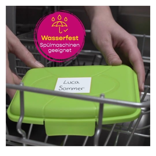 Das Bild zeigt einen grünen Behälter, der in eine Spülmaschine gestellt wird. Auf dem Behälter befindet sich ein Etikett mit dem Namen 'Luca Sommer', und darüber ist ein pinkfarbenes, rundes Logo, das anzeigt 'wasserfest und spülmaschinengeeignet'.