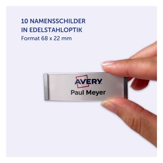 Das Bild zeigt eine Hand, die ein Namensschild mit dem Namen 'Paul Meyer' und der Marke 'Avery' hält. Das Schild hat ein metallisches Aussehen und die Maße von 68 x 22 mm.