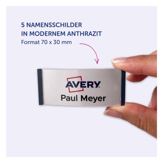 Das Bild zeigt eine Hand, die ein Namensschild hält, auf dem 'Avery Paul Meyer' in einer modernen anthrazitfarbenen Schrift steht. Es ist als Teil eines Sets von fünf Namensschildern mit den Abmessungen 70 x 30 mm gekennzeichnet.