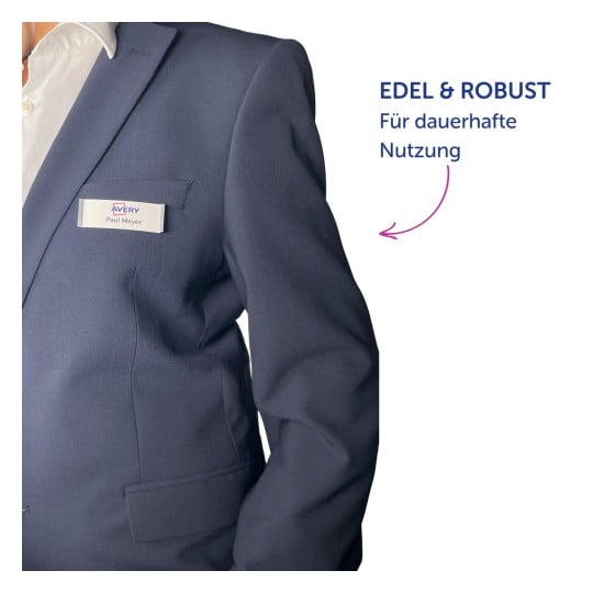 Das Bild zeigt einen Mann in einem marineblauen Anzug mit einem Namensschild, auf dem 'Paul Meyer' steht. Im Hintergrund ist Text zu sehen, der 'EDEL & ROBUST' und 'Für dauerhafte Nutzung' lautet.