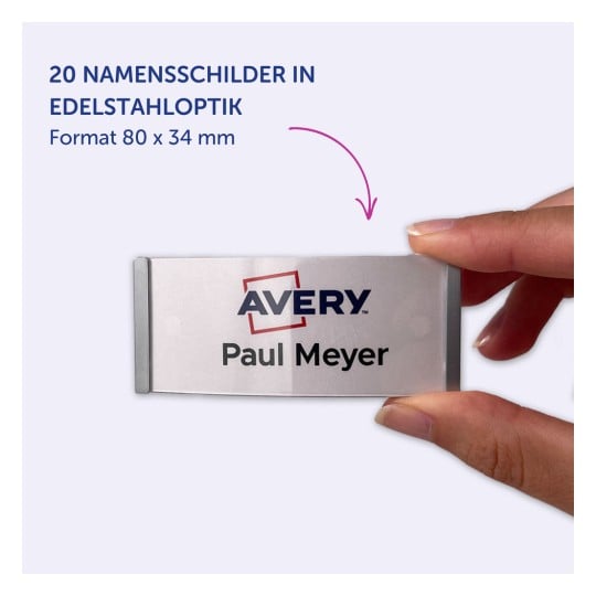 Das Bild zeigt ein Namensschild, das in einer Hand gehalten wird, mit der Beschriftung 'Avery' und dem Namen 'Paul Meyer' darauf. Es zeigt an, dass es 20 Namensschilder in Edelstahloptik gibt, die 80 x 34 mm messen.