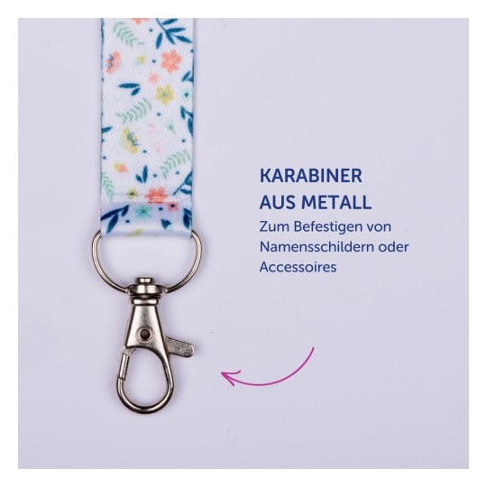Das Bild zeigt einen Metallkarabiner, der an einem Stoffband mit Blumenmuster befestigt ist, sowie einen Text, der seine Verwendung zur Befestigung von Namensschildern oder Accessoires beschreibt.