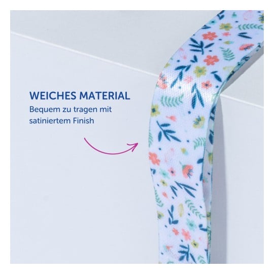 Das Bild zeigt ein Band oder eine Schleife aus weichem Material mit einem Blumenmuster, zusammen mit dem Text 'WEICHES MATERIAL' und Informationen über Komfort und Satin-Finish.