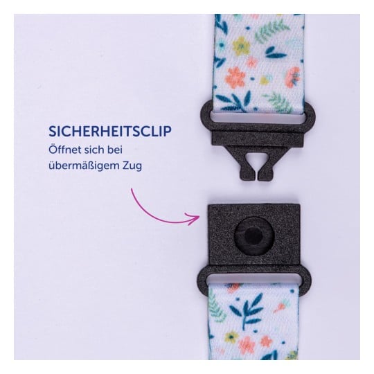 Das Bild zeigt einen Sicherheitsclip, der mit einem bunten Riemen mit Blumenmustern und einem deutschen Text zu seiner Funktion versehen ist.