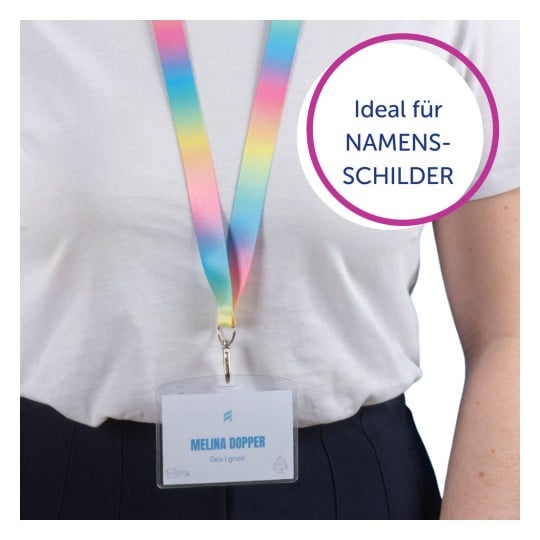 Das Bild zeigt eine Person, die ein buntes Schlüsselband mit einem Namensschild trägt, auf dem 'Melina Doppler, Designerin' steht. Das Schlüsselband hat einen Regenbogenfarbverlauf, und das Schild ist transparent mit einem blauen Namensschild.