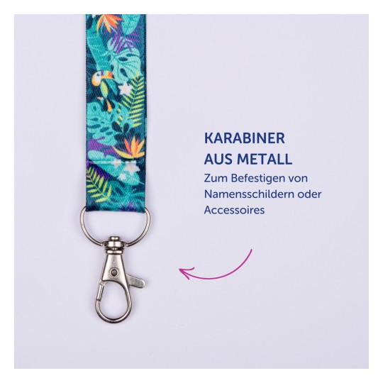 Das Bild zeigt ein buntes Lanyard mit einem Metallclip, ideal zum Befestigen von Namensschildern oder Accessoires. Das Design umfasst tropische Elemente wie Blätter und Vögel. Der Text an der Seite gibt an, wofür es verwendet wird.