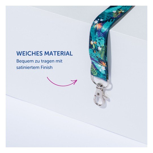 Das Bild zeigt ein buntes Lanyard mit tropischem Muster, das sein weiches Material zur Geltung bringt. Es ist an einem Haken befestigt und wird als angenehm zu tragen mit einer Satin-Oberfläche beschrieben. Der danebenstehende Text betont seine Weichheit und seinen Tragekomfort.
